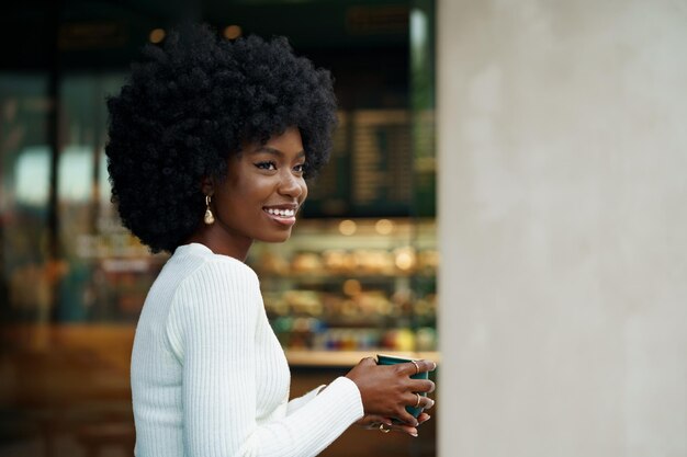 Porträt einer jungen Afrikanerin mit Afrofrisur, die im städtischen Hintergrund lächelt