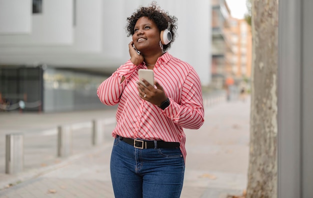 Porträt einer jungen Afroamerikanerin plus Größe, die Musik vom Smartphone mit Kopfhörern hört