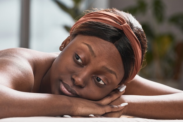 Porträt einer jungen afroamerikanischen Frau, die auf einem Massagetisch liegt und Schönheitspflege genießt, Kopierraum