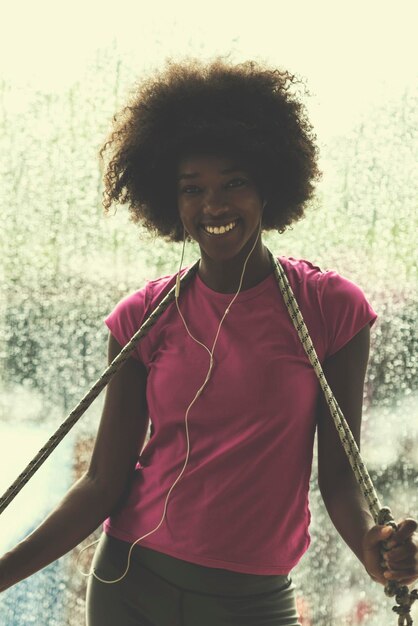 Foto porträt einer jungen afroamerikanischen frau im fitnessstudio in der trainingspause, während sie musik über kopfhörer hört und regnerischen tag und schlechtes wetter im freien tanzt