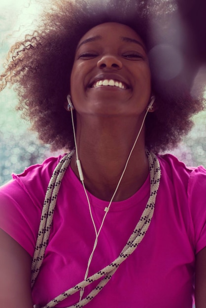 porträt einer jungen afroamerikanischen frau im fitnessstudio in der trainingspause, während sie musik über kopfhörer hört und regnerischen tag und schlechtes wetter im freien tanzt
