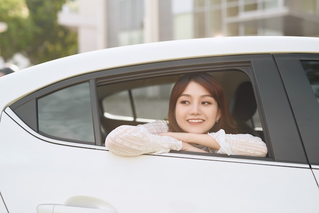 Porträt einer jungen asiatischen Frau, die durch das Fenster in die Kamera schaut und auf dem Rücksitz im Auto sitzt