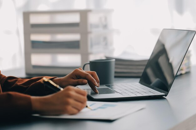 Porträt einer jungen asiatischen Frau, die freiberuflich an einem Computer in einem modernen Büro arbeitet. Sie macht Buchhaltungsanalysen, Berichte, Immobilieninvestitionsdaten, Konzepte für Finanz- und Steuersysteme.