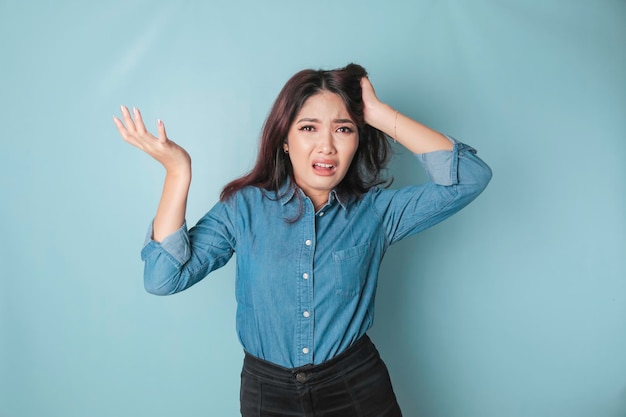Porträt einer jungen asiatischen Frau, die von blauem Hintergrund isoliert ist und sich frustriert über einen hilflosen Gesichtsausdruck fühlt