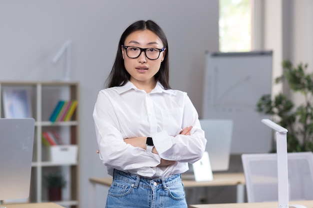 Porträt einer jungen asiatischen Geschäftsfrau ein Arbeiter im Büro mit verschränkten Armen in die Kamera schaut