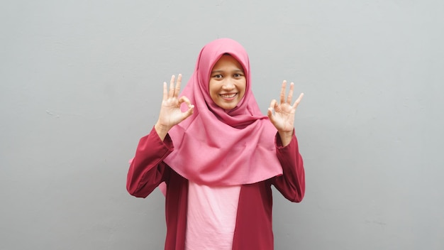 Porträt einer jungen asiatischen muslimischen Dame mit Hijab zeigt Daumen hoch Geste, lächelt glückliches Gesicht, genehmigtes OK-Zeichen
