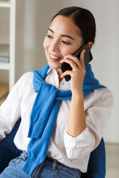 Porträt einer jungen asiatischen Sekretärin, die lächelt und am Handy spricht, während sie im Büro arbeitet