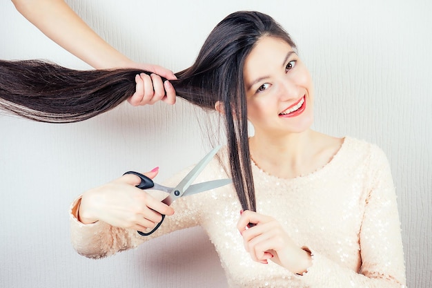 Porträt einer jungen attraktiven brünetten Frau mit langen schwarzen Haaren und Make-up in einer rosa Kleiderschere mit Scherenhaarschnitt im Friseurladen