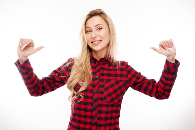 Porträt einer jungen blonden Frau, die lächelt und selbstbewusst aussieht und mit isolierten Fingern auf den weißen Hintergrund zeigt. Sie entscheidet sich für das Konzept des Selbstwertgefühls