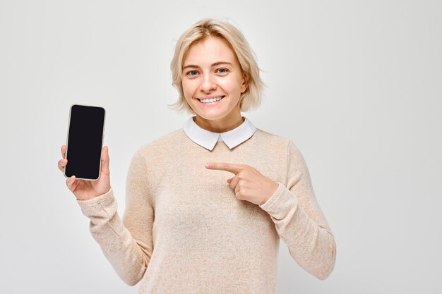 Foto porträt einer jungen blonden frau mit einem leeren handybildschirm und einem aufgeregten gesicht person mit smartphone auf weißem hintergrund