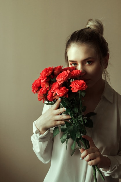 Porträt einer jungen blonden Frau mit rotem Make-up und einem Strauß Rosen