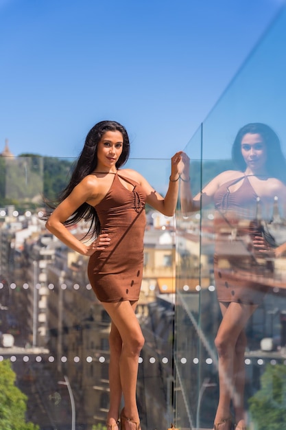 Porträt einer jungen brünetten auf einer hotelterrasse mit der stadt im hintergrund, die sich an die glasscheibe lehnt