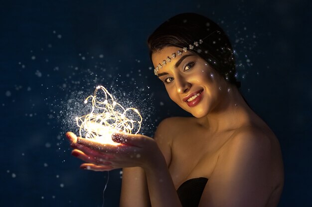 Porträt einer jungen brünetten Frau, die einen glühenden Ball der LED-Lichter hält.