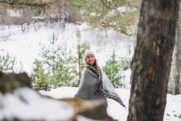 Porträt einer jungen brünetten Schönheit mit Hut und grauem Poncho im Winterwald