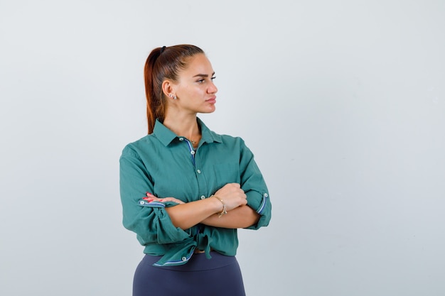 Porträt einer jungen Dame, die mit verschränkten Armen steht, während sie im grünen Hemd wegschaut und nachdenkliche Vorderansicht schaut