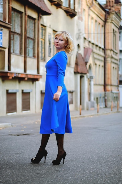 Porträt einer jungen eleganten blonden Frau mit blauen Augen, die in den Straßen der Herbststadt spaziert. Blaues Kleid