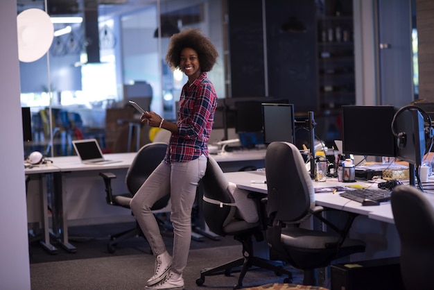 Porträt einer jungen, erfolgreichen afroamerikanischen, schönen Frau, die es genießt, eine gute und freudige Zeit zu verbringen, während sie in einem großen, modernen Büro arbeitet