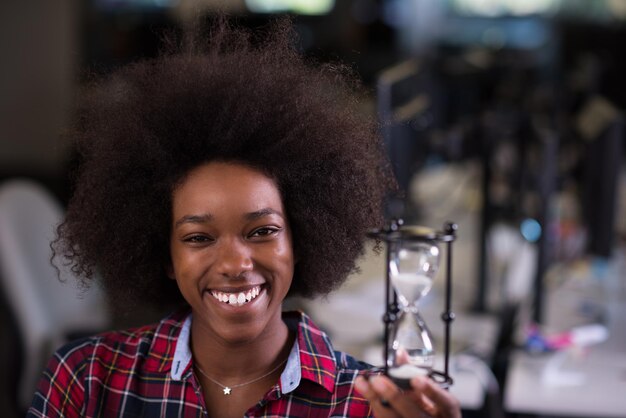 Porträt einer jungen, erfolgreichen afroamerikanischen, schönen Frau, die es genießt, eine gute und freudige Zeit zu verbringen, während sie in einem großen, modernen Büro arbeitet