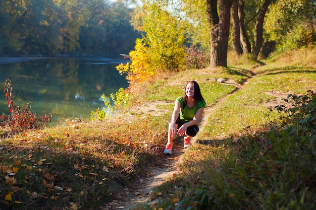 Porträt einer jungen fitten Frau, die sitzt, während ihr Lauftraining auf dem Weg im Stadtpark ruht.