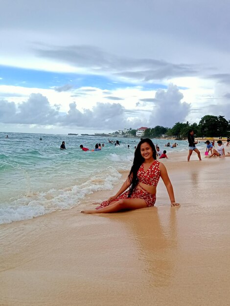 Foto porträt einer jungen frau, die am strand gegen den himmel sitzt