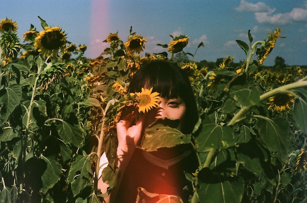 Porträt einer jungen Frau, die auf einem Bauernhof inmitten von Sonnenblumen schleifte