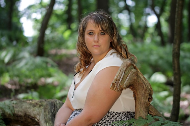 Porträt einer jungen Frau, die auf einem Baumstamm im Wald sitzt
