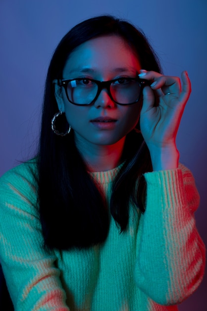 Porträt einer jungen Frau, die Brille im roten und blauen Licht trägt und berührt
