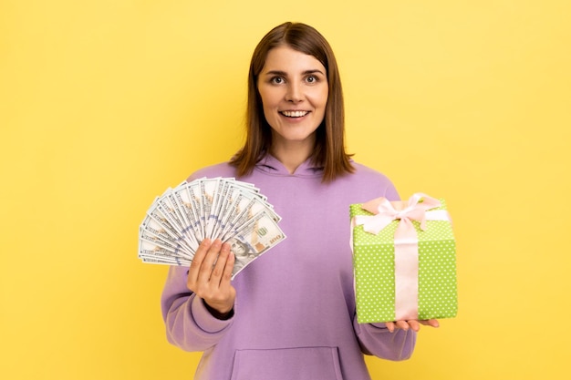 Porträt einer jungen Frau, die ein Geschenk vor gelbem Hintergrund hält