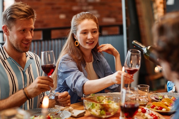 Porträt einer jungen Frau, die ein Glas Wein genießt, während sie mit Freunden auf einer Dinnerparty feiert