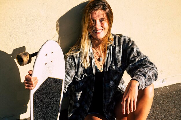 Foto porträt einer jungen frau, die ein skateboard an der wand hält