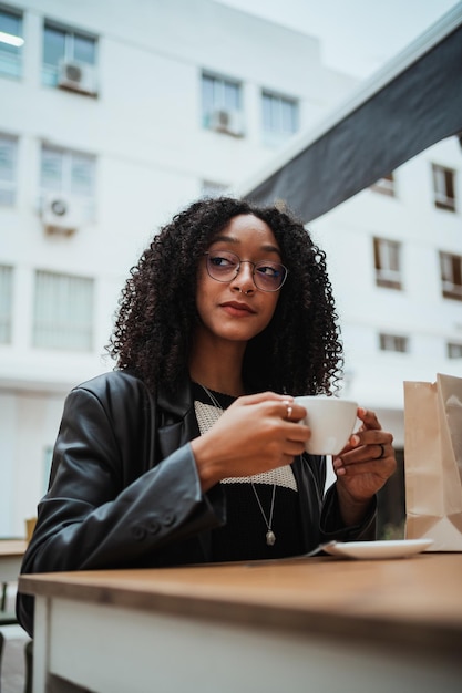 Porträt einer jungen Frau, die eine heiße Kaffeetasse hat, während sie sich auf einer Caféterrasse ausruht