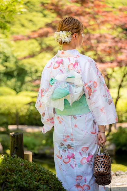 Foto porträt einer jungen frau, die einen yukata-sommerkimono mit weichem, verschwommenem hintergrund im japanischen garten trägt