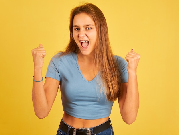 Porträt einer jungen Frau, die feiert, ein Gewinner auf gelber Wand zu sein