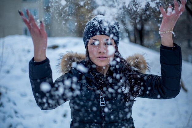 Porträt einer jungen Frau, die im Freien mit Schnee spielt