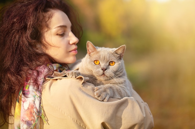 Porträt einer jungen Frau, die im Herbstpark mit einer Katze im Arm abends spaziert