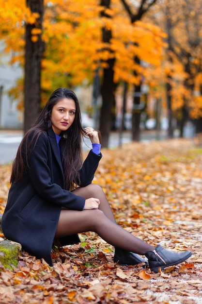 Porträt einer jungen Frau, die im Herbstpark sitzt