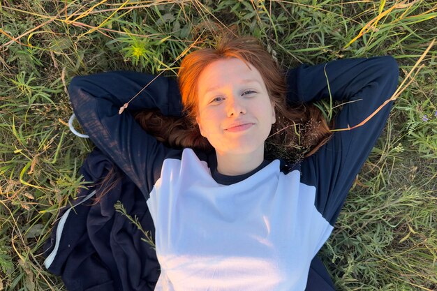 Foto porträt einer jungen frau, die im warmen sommerwetter bei sonnenuntergang im gras liegt