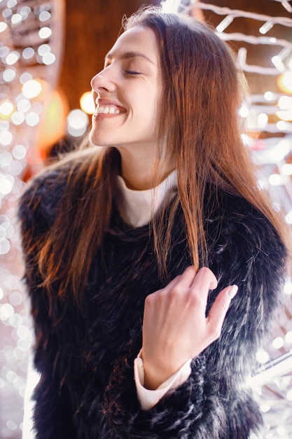 Porträt einer jungen Frau, die in der Nähe von weißer Weihnachtsbeleuchtung posiert