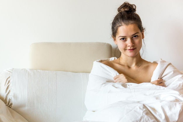 Porträt einer jungen Frau, die in eine Decke gewickelt ist und zu Hause auf dem Sofa sitzt
