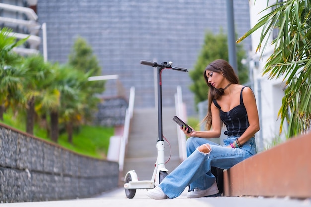 Porträt einer jungen Frau, die mit einem Elektroroller in der Stadt sitzt und eine Nachricht tippt