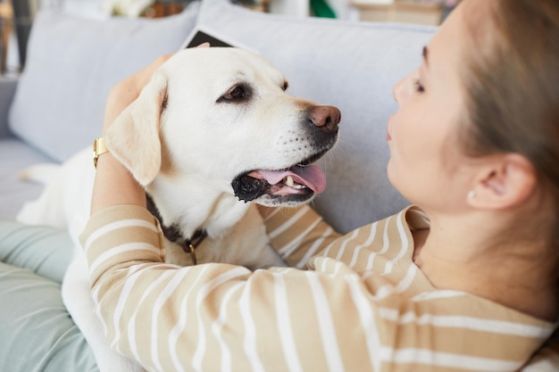 Porträt einer jungen Frau, die mit Hund kuschelt, während sie zu Hause auf der Couch liegt