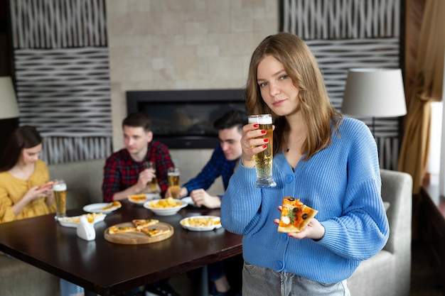 Porträt einer jungen Frau, die Pizza und Bier in einer Kneipe hält