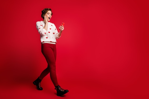 Porträt einer jungen Frau, die stilvollen trendigen Pullover lokalisiert auf roter Wand trägt