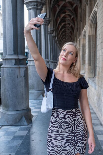 Porträt einer jungen Frau, die vor einem historischen Gebäude in einer europäischen Stadt steht und ein Selfie macht