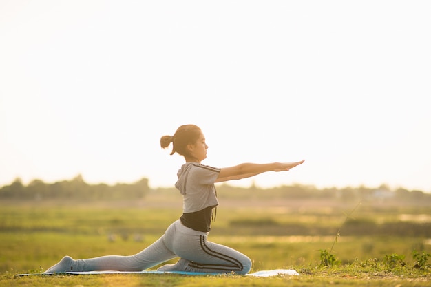 Porträt einer jungen Frau, die Yoga draußen im sonnigen hellen Licht durchführt.