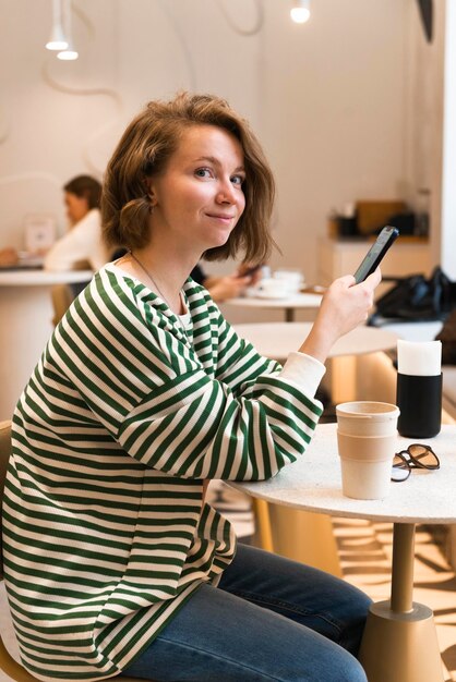 Foto porträt einer jungen frau im café mit handy und blick in die kamera