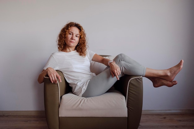 Porträt einer jungen Frau im weißen T-Shirt, die auf dem Sofa sitzt. Hochwertiges Foto