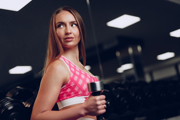 Porträt einer jungen Frau in der Sportbekleidung, die in einem dunklen Fitnessstudio aufwirft