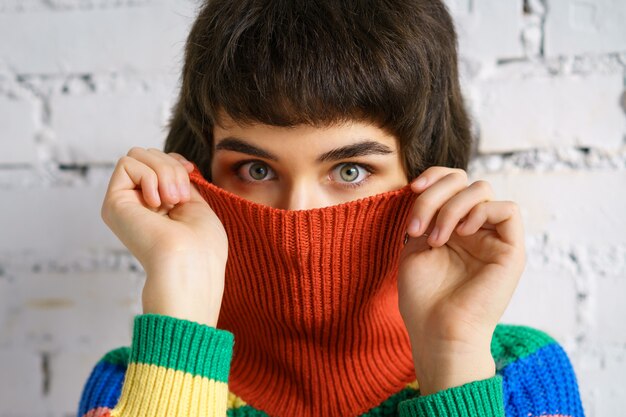 Porträt einer jungen Frau in einem bunten Pullover, die ihr Gesicht mit einem Pullover bedeckt. Das Konzept der Schüchternheit