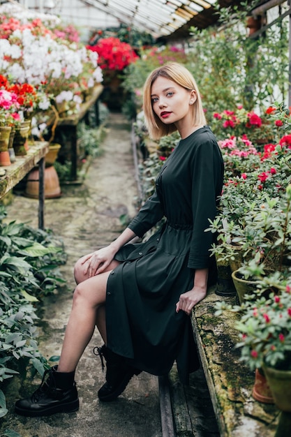 Porträt einer jungen Frau in einem grünen Kleid in einem Gewächshaus mit roten und rosa blühenden Azaleen